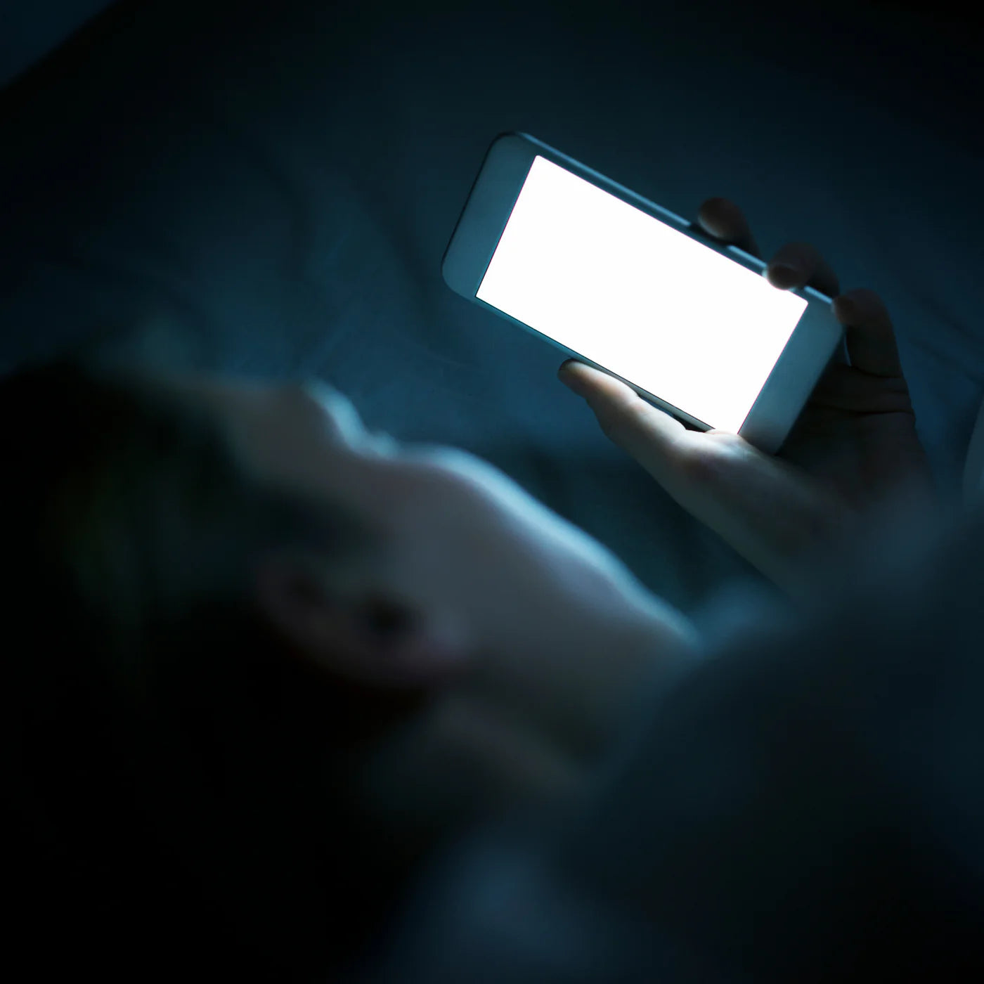 Persoon ligt in bed en kijkt naar een fel verlichte smartphone, blootgesteld aan blauw licht.